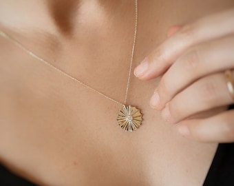 May include: A gold necklace with a delicate chain and a pendant shaped like a sunburst with a small diamond in the center.