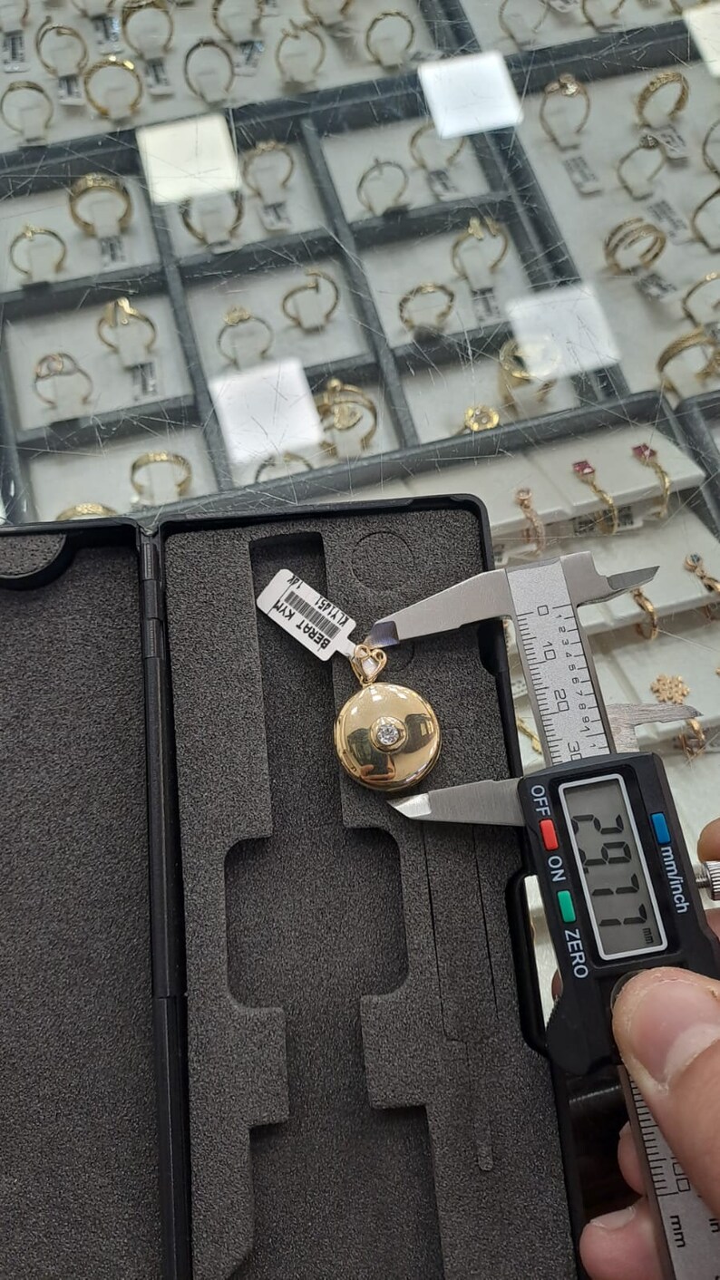 K&ouml;nnte beinhalten: Ein goldener Anh&auml;nger mit einem runden, kreisf&ouml;rmigen Design und einem einzelnen Diamanten in der Mitte. Der Anh&auml;nger wird mit einer digitalen Schieblehre gemessen, die 29,77 mm anzeigt. Der Anh&auml;nger ist mit "Berat KYM" und "KLY1451" beschriftet.