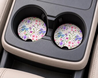 Könnte beinhalten: Zwei runde Auto-Getränkehalter-Untersetzer mit weißem Hintergrund und einem bunten Blumenmuster aus kleinen rosa, violetten und blauen Blüten mit grünen Stielen und Blättern. Jeder Untersetzer hat eine kleine halbkreisförmige Aussparung.