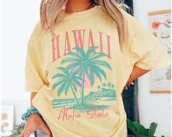 Peut inclure: Un t-shirt jaune avec un imprimé graphique de palmiers et le texte "Hawaii Aloha State".