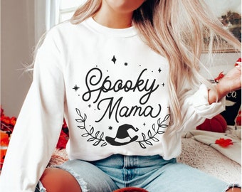 May include: White long-sleeved sweatshirt with the text "Spooky Mama" in black script with a witch's hat and leaves.