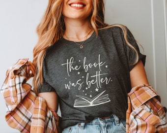 May include: A dark gray t-shirt with the text "the book was better." in white lettering. The shirt features a white outline of an open book with stars around it.