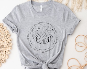 May include: Gray t-shirt with a black and white graphic design of a crescent moon, mountains, and stars. The text "It is the stars, the stars above us, govern our conditions - William Shakespeare" is printed around the graphic.
