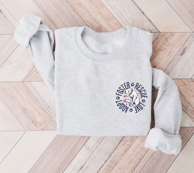 May include: A gray sweatshirt with a white dog illustration and the text "Adopt Foster Rescue Love" in a circle around the dog.