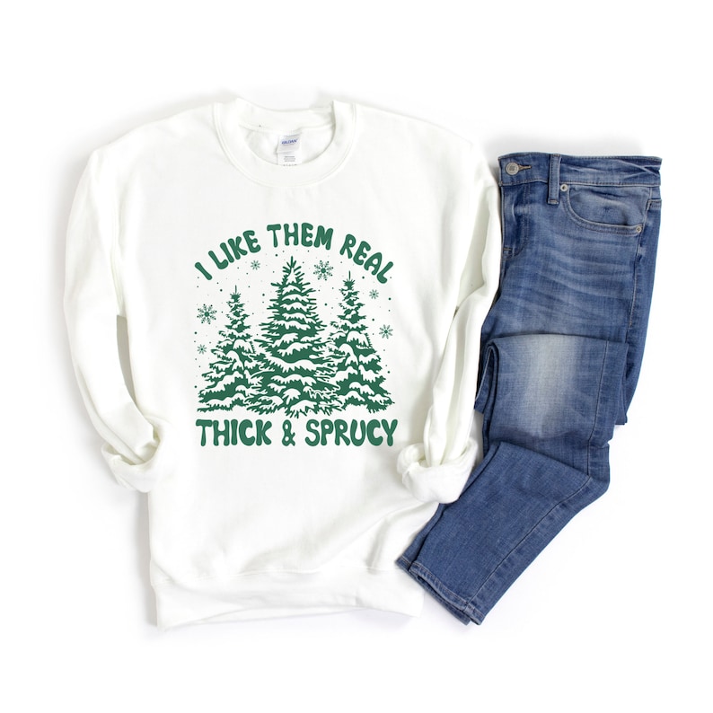 May include: White sweatshirt with a green graphic of three snow-covered pine trees and the text "I like them real thick & sprucy".