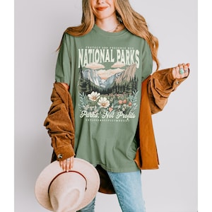 K&ouml;nnte beinhalten: Gr&uuml;nes T-Shirt mit einem grafischen Aufdruck einer Berglandschaft und Blumen. Der Text "Protect and Preserve Our National Parks" ist in Wei&szlig; &uuml;ber dem Grafikdruck gedruckt. Der Text "Parks, Not Profits" ist in Wei&szlig; unter dem Grafikdruck gedruckt. Der Text "Explore, Respect, Resist" ist in Wei&szlig; unter dem Text "Parks, Not Profits" gedruckt.