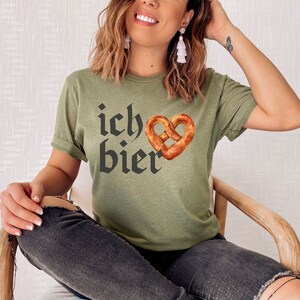 Op de afbeelding: Een groen T-shirt met de tekst "ich bier" in zwarte gotische letter en een hartvormige pretzel.