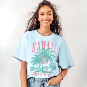 May include: A light blue t-shirt with a vintage-style graphic of palm trees and the text "Hawaii Aloha State".