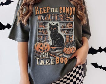 May include: Dark grey t-shirt with a Halloween-themed graphic. The design features a black cat sitting on books in front of a bookshelf, with pumpkins and the text "Keep the Candy, I'll Take Boo".