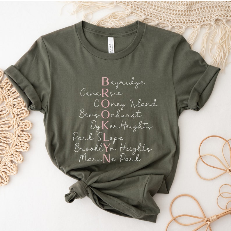 May include: A green t-shirt with the word "BROOKLYN" spelled out vertically using the names of different neighborhoods in Brooklyn, New York. The word "BROOKLYN" is written in pink.