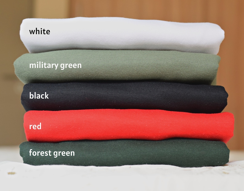 May include: A stack of five folded t-shirts in different colors: white, military green, black, red, and forest green.