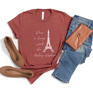 K&ouml;nnte beinhalten: Ein maronfarbenes T-Shirt mit einer wei&szlig;en Grafik des Eiffelturms und dem Zitat "Paris ist immer eine gute Idee. - Audrey Hepburn".