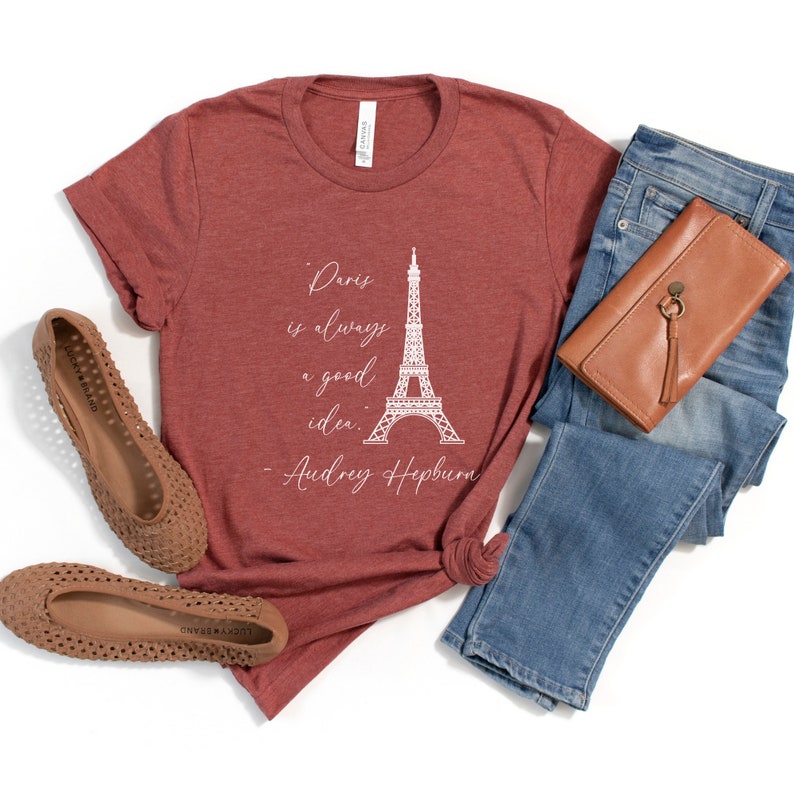 K&ouml;nnte beinhalten: Ein maronfarbenes T-Shirt mit einer wei&szlig;en Grafik des Eiffelturms und dem Zitat "Paris ist immer eine gute Idee. - Audrey Hepburn".