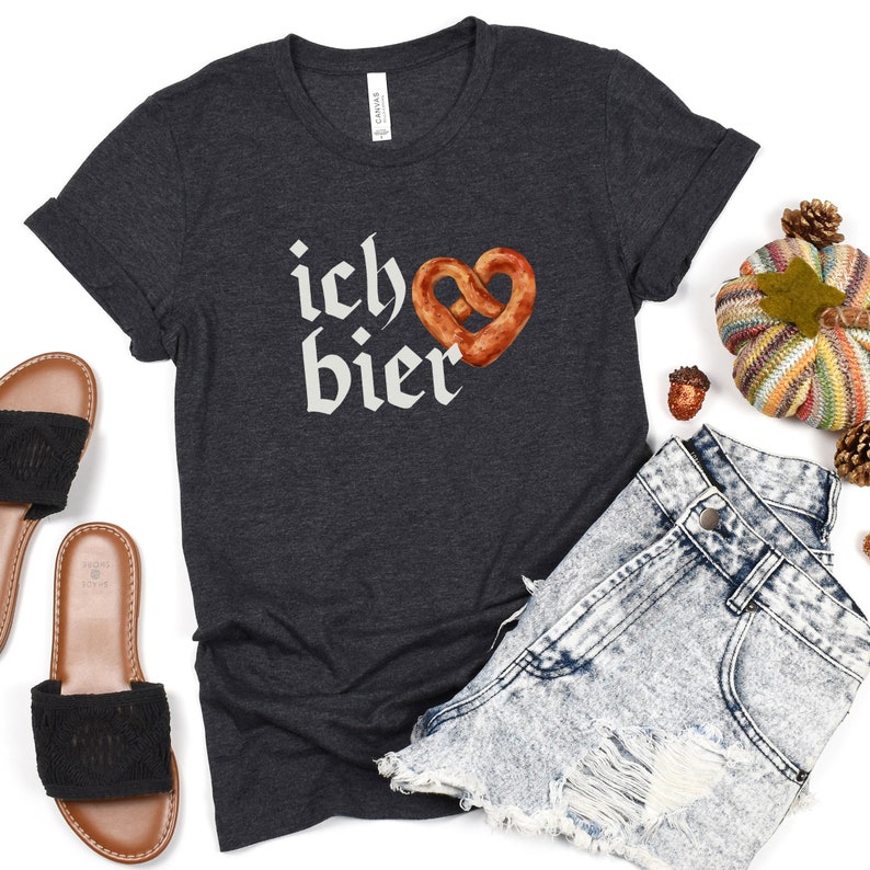 Op de afbeelding: Een donkergrijs T-shirt met de tekst "ich &hearts; bier" in witte letters en een bruine pretzel in de vorm van een hart.
