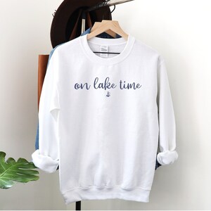 Puede incluir: Sudadera blanca con el texto "on lake time" en escritura azul con un peque&ntilde;o s&iacute;mbolo de ancla debajo del texto.