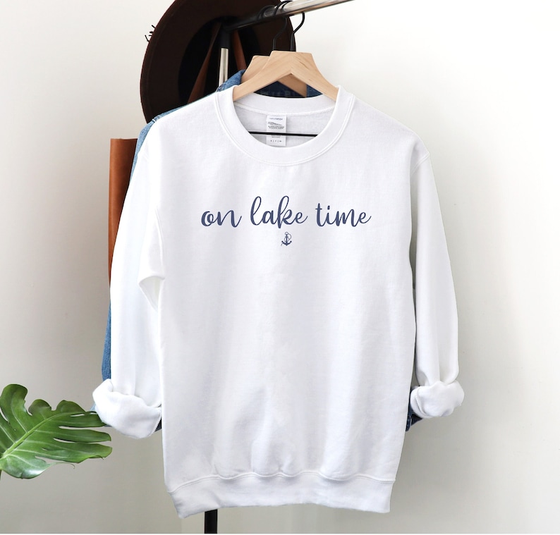 Puede incluir: Sudadera blanca con el texto "on lake time" en escritura azul con un peque&ntilde;o s&iacute;mbolo de ancla debajo del texto.
