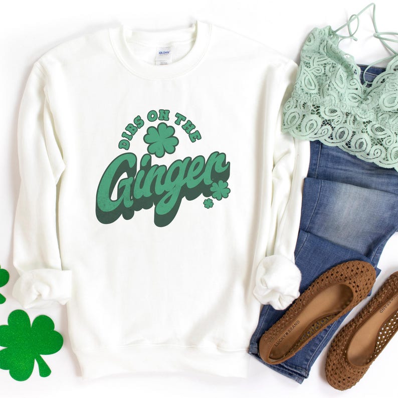 K&ouml;nnte beinhalten: Ein wei&szlig;es Sweatshirt mit dem gr&uuml;nen Schriftzug "Dibs on the Ginger" und Kleeblatt-Akzenten. Das Bild zeigt auch braune Ballerinas, eine blaue Jeans und ein gr&uuml;nes Spitzentop. Das Sweatshirt hat ein St. Patrick's Day-Thema.