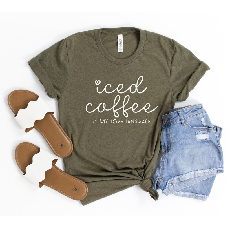 Puede incluir: Una camiseta verde con el texto "iced coffee is my love language" en letras blancas. La camiseta se combina con pantalones cortos de mezclilla y sandalias blancas.