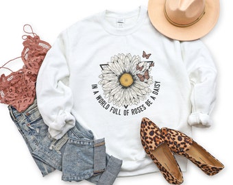 May include: White sweatshirt featuring a graphic of a daisy and butterflies. The text "In a world full of roses be a daisy" is printed on the sweatshirt.
