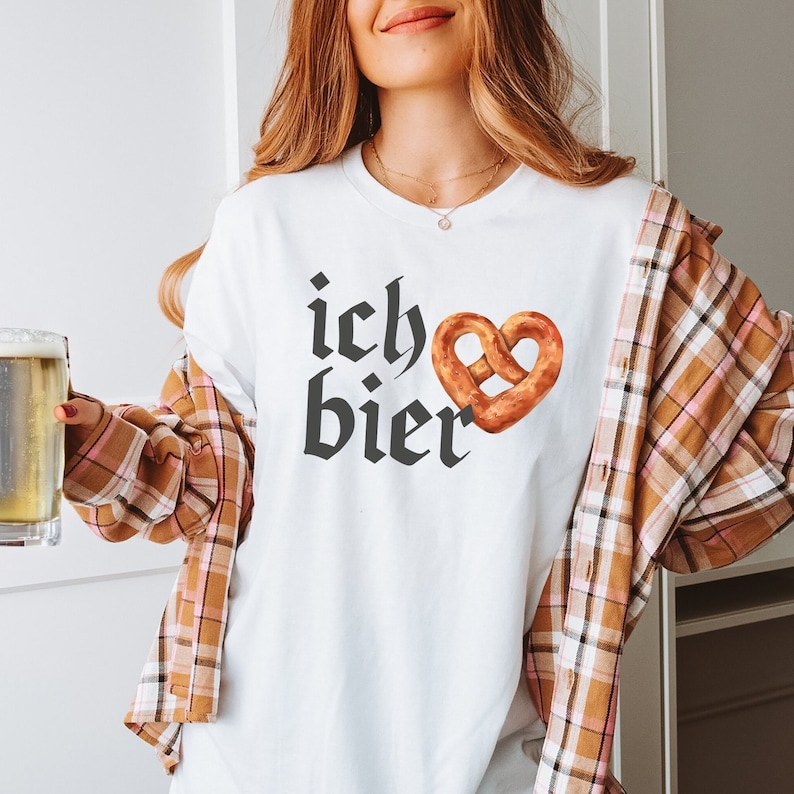 Op de afbeelding: Wit T-shirt met de tekst "ich bier" in zwarte gotische letter en een bruine pretzel in de vorm van een hart.