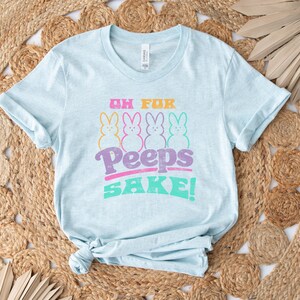 May include: Light blue t-shirt with a graphic of four pastel-colored Peeps and the text "Oh For Peeps Sake!"