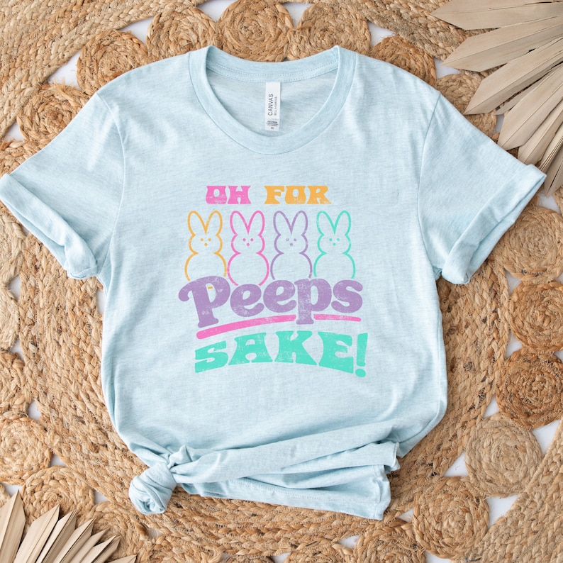 May include: Light blue t-shirt with a graphic of four pastel-colored Peeps and the text "Oh For Peeps Sake!"