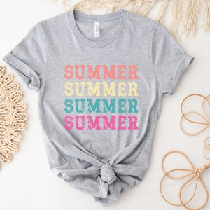 May include: A gray t-shirt with the word "SUMMER" printed four times in a stacked design. The word is in a distressed font and features the colors peach, yellow, teal, and pink. The shirt is knotted at the waist.