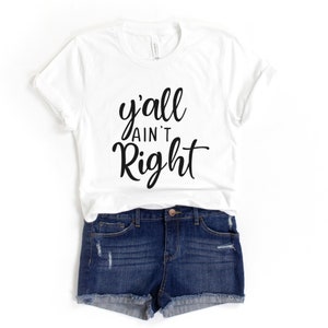 May include: White t-shirt with black text that reads "y'all ain't right". The shirt is being modelled with denim shorts.
