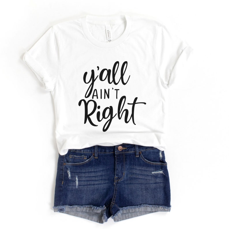 May include: White t-shirt with black text that reads "y'all ain't right". The shirt is being modelled with denim shorts.