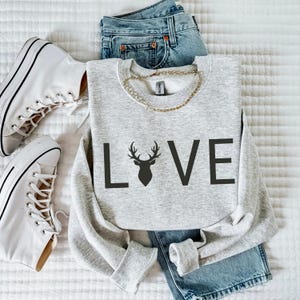 May include: A gray sweatshirt with the word "LOVE" printed on the front. The "O" in LOVE is replaced with a silhouette of a deer head with antlers.