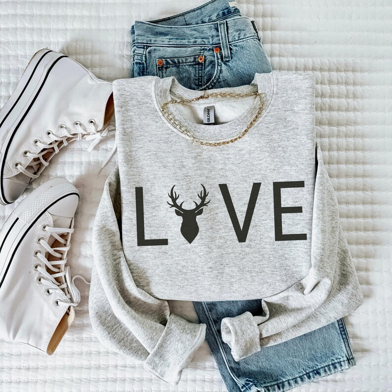 May include: A gray sweatshirt with the word "LOVE" printed on the front. The "O" in LOVE is replaced with a silhouette of a deer head with antlers.