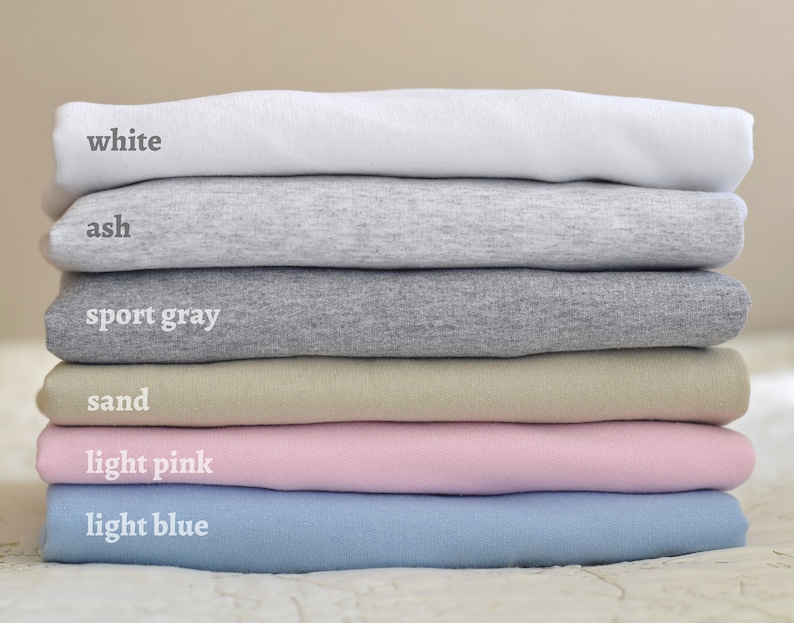 Puede incluir: Pila de seis camisetas de diferentes colores: blanco, ceniza, gris deportivo, arena, rosa claro y azul claro.
