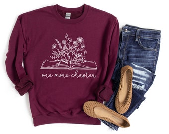 Peut inclure: Sweat-shirt bordeaux avec un graphique blanc d'un livre ouvert avec des fleurs qui poussent. Le texte "one more chapter" est imprimé sous le livre.