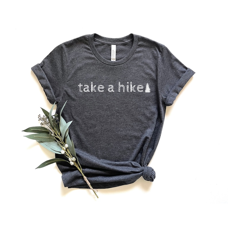 May include: A dark heather gray t-shirt with the text "take a hike" and a stylized pine tree graphic in white.