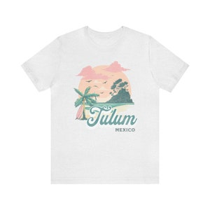 May include: White t-shirt with a graphic of a sunset over a beach with a palm tree and surfboard. The text "Tulum Mexico" is printed below the graphic.