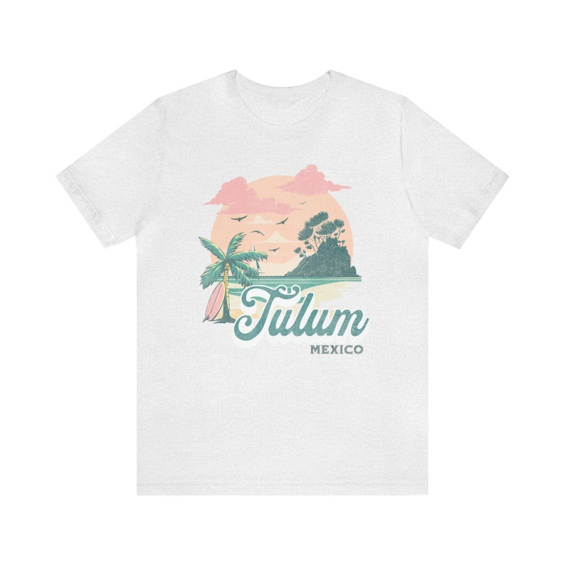 May include: White t-shirt with a graphic of a sunset over a beach with a palm tree and surfboard. The text "Tulum Mexico" is printed below the graphic.