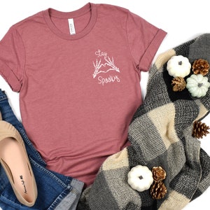 May include: A maroon t-shirt with a white graphic of skeleton hands making a heart shape with the text "Stay Spooky" on the front.