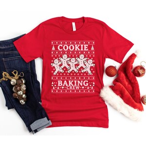 May include: Red Christmas sweater with a white gingerbread man design and the text "Cookie Baking Crew".