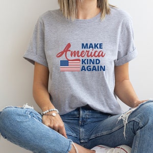 May include: A grey t-shirt with the text "Make America Kind Again" in red and blue lettering. An American flag graphic is centered above the text.
