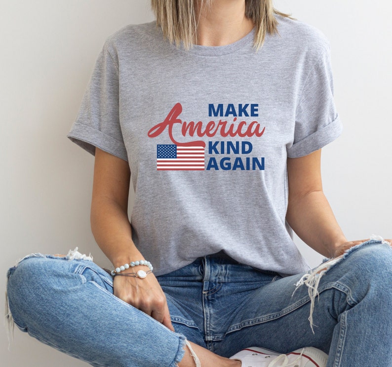 May include: A grey t-shirt with the text "Make America Kind Again" in red and blue lettering. An American flag graphic is centered above the text.