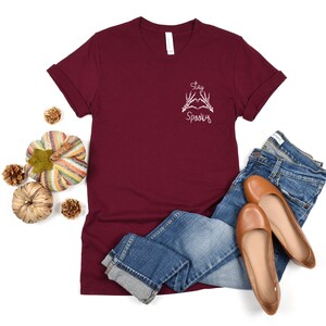 May include: Burgundy t-shirt with a white graphic of two skeleton hands making a heart shape with the text "Stay Spooky" on the front.