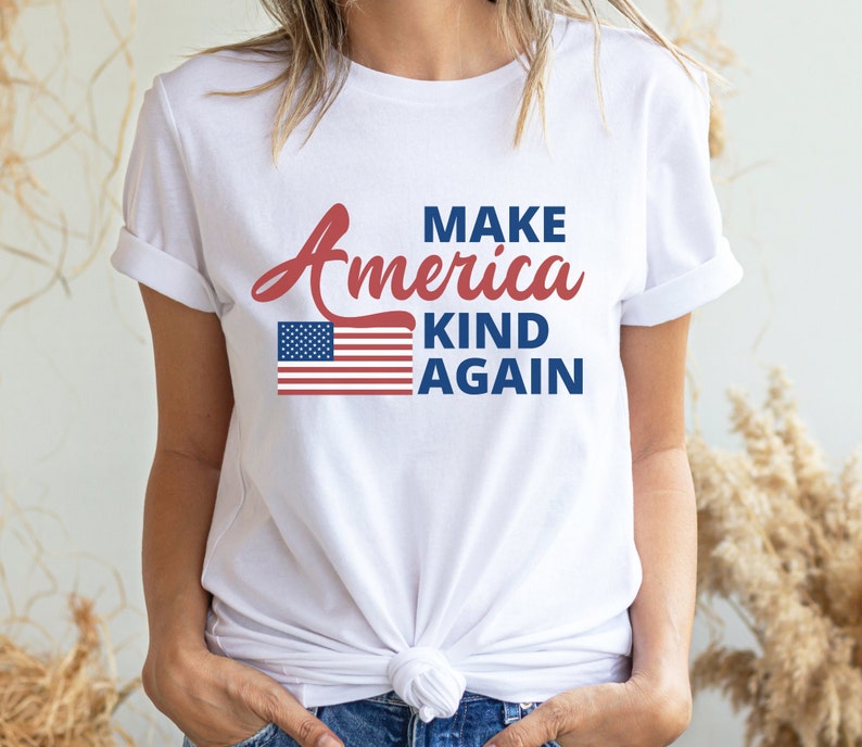 May include: White t-shirt with a red, white, and blue American flag graphic and the text "Make America Kind Again".