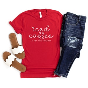 Puede incluir: Camiseta roja con texto blanco que dice "iced coffee is my love language". La camiseta se combina con jeans azules y sandalias marrones.