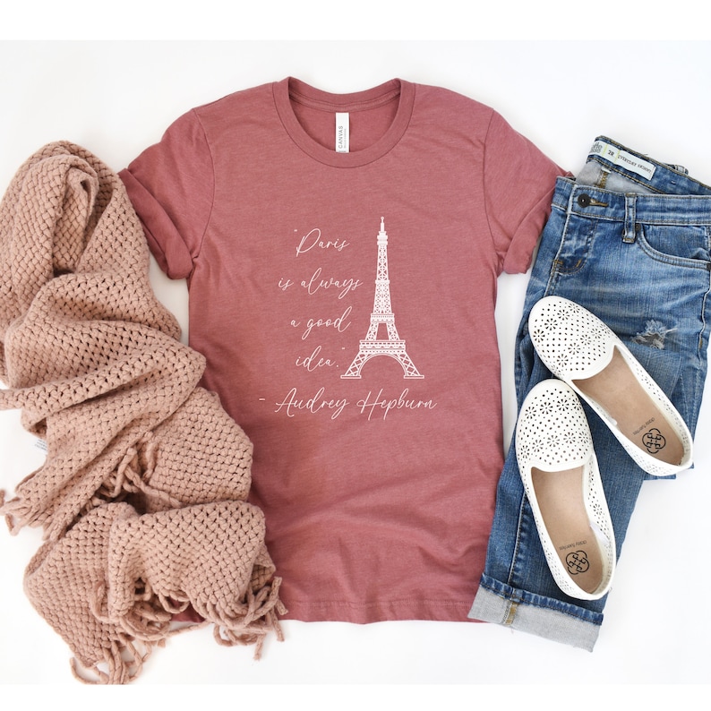 K&ouml;nnte beinhalten: Ein maronfarbenes T-Shirt mit einer wei&szlig;en Grafik des Eiffelturms und dem Zitat "Paris ist immer eine gute Idee. - Audrey Hepburn".