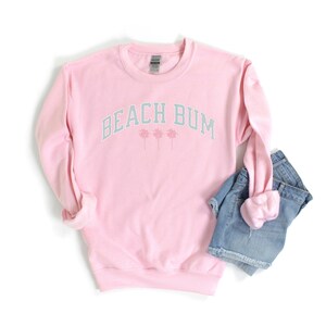 Pu&ograve; includere: Felpa rosa con la scritta "Beach Bum" in azzurro con tre palme rosa sotto.