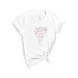 May include: White t-shirt with a pink and gold line drawing of a bouquet of flowers in an ice cream cone.