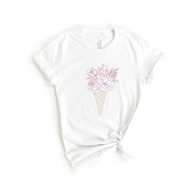 May include: White t-shirt with a pink and gold line drawing of a bouquet of flowers in an ice cream cone.