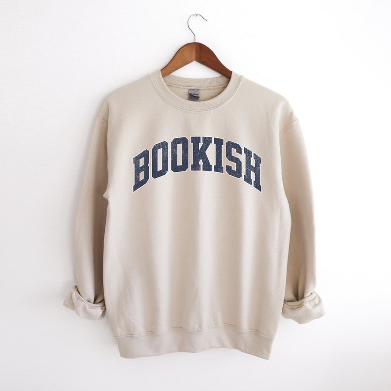 May include: A beige sweatshirt with the word "BOOKISH" printed in a navy blue arch across the front.