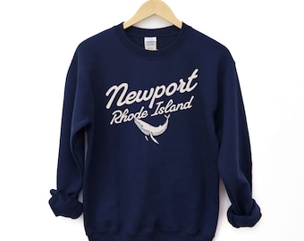 May include: A navy blue sweatshirt with a white graphic of a whale and the text "Newport Rhode Island" in a white cursive font.