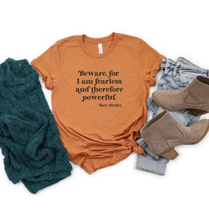Puede incluir: Una camiseta de color &oacute;xido con una cita de Mary Shelley que dice: "Beware, for I am fearless and therefore powerful."